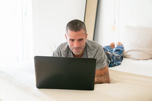 Free Man Lying on Bed While Using Laptop Stock Photo