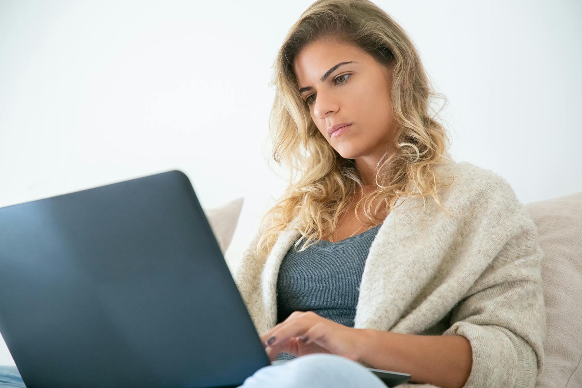 Blonde woman working on a laptop, deeply focused in a cozy home setting.