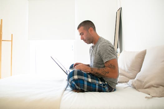 Casual man in pajamas using laptop while working remotely at home.