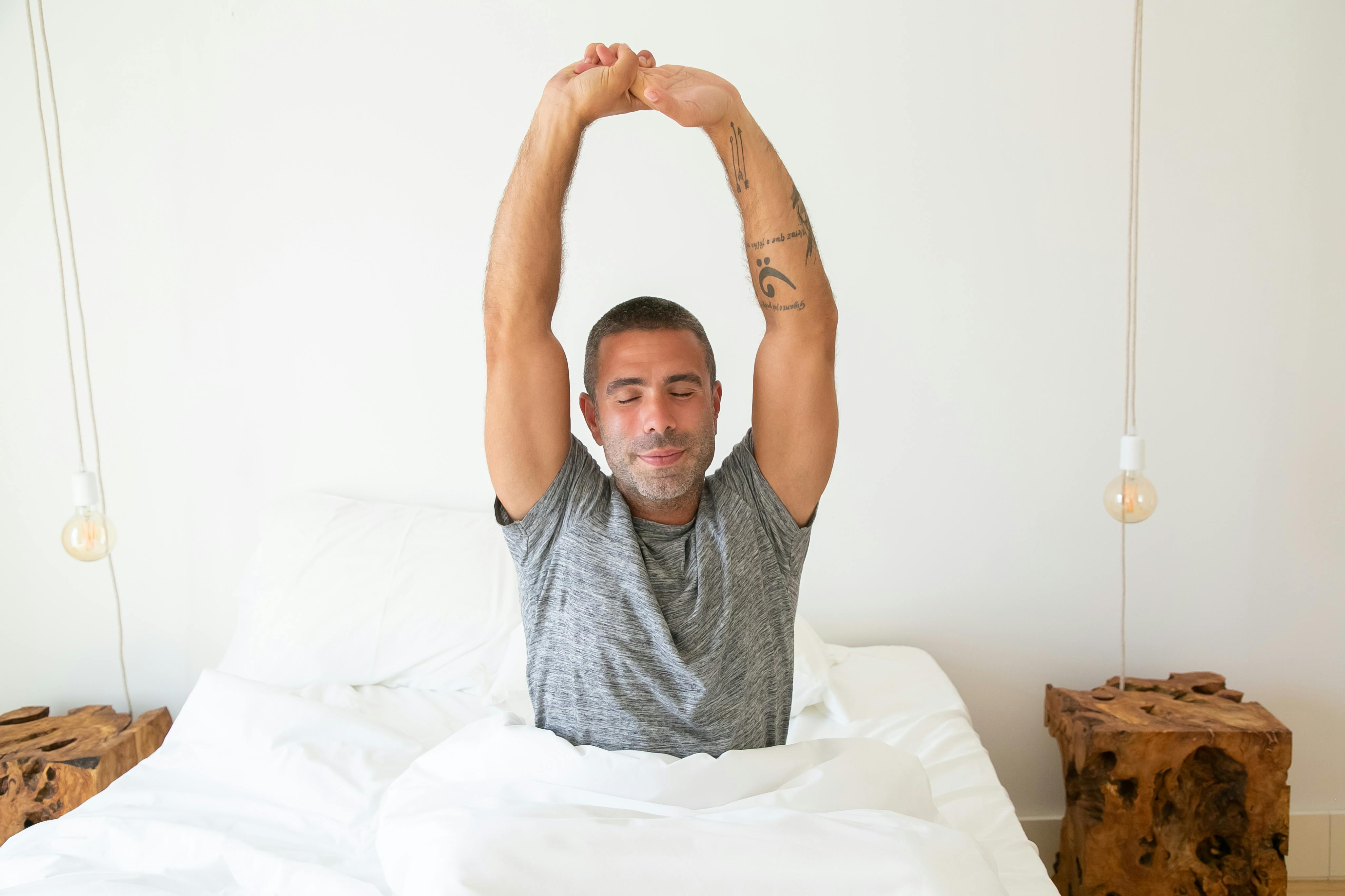 A man stretching his arms while waking up in bed, starting the morning with energy.