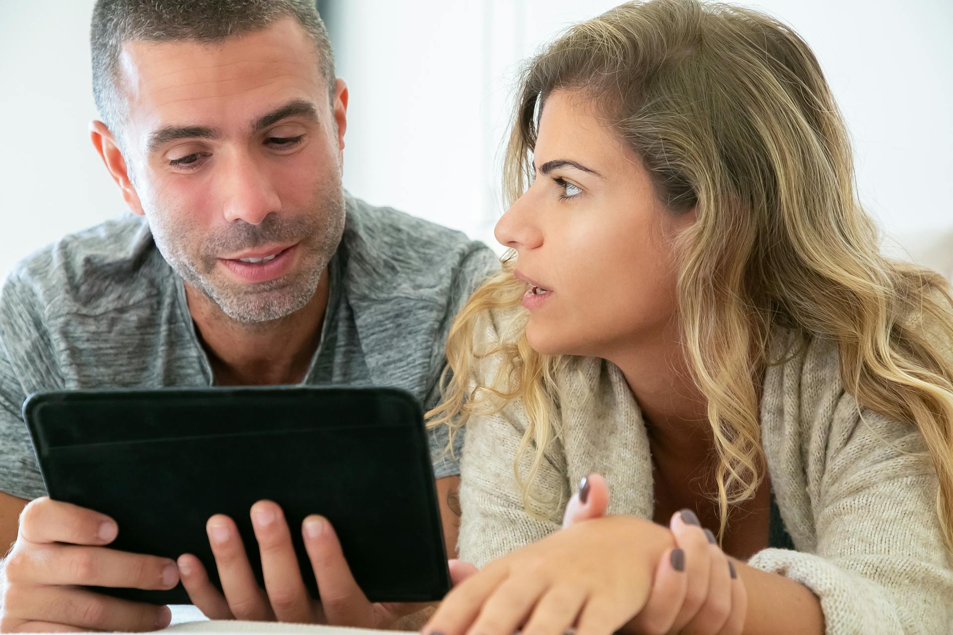 A couple engaging in conversation while using a tablet at home, focusing on digital collaboration.