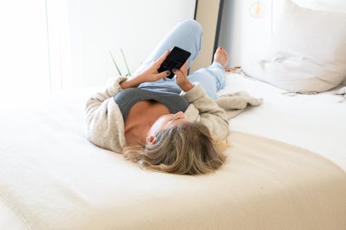 Woman Lying on Bed While Using Cellphone
