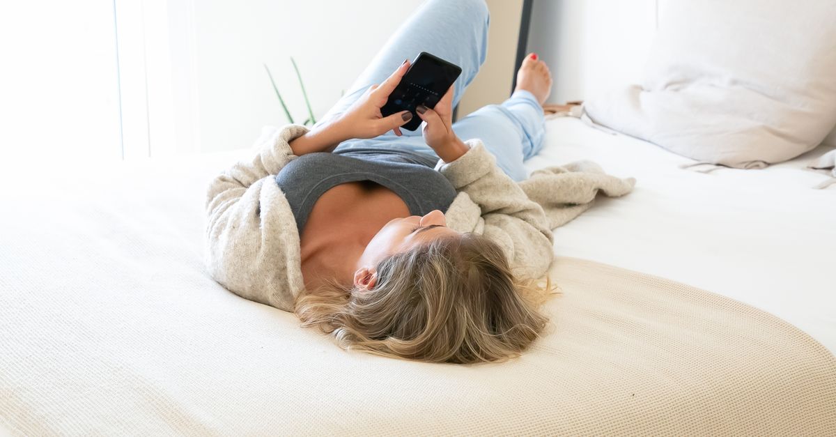 person lying in bed with phone, cozy blankets, soft lighting