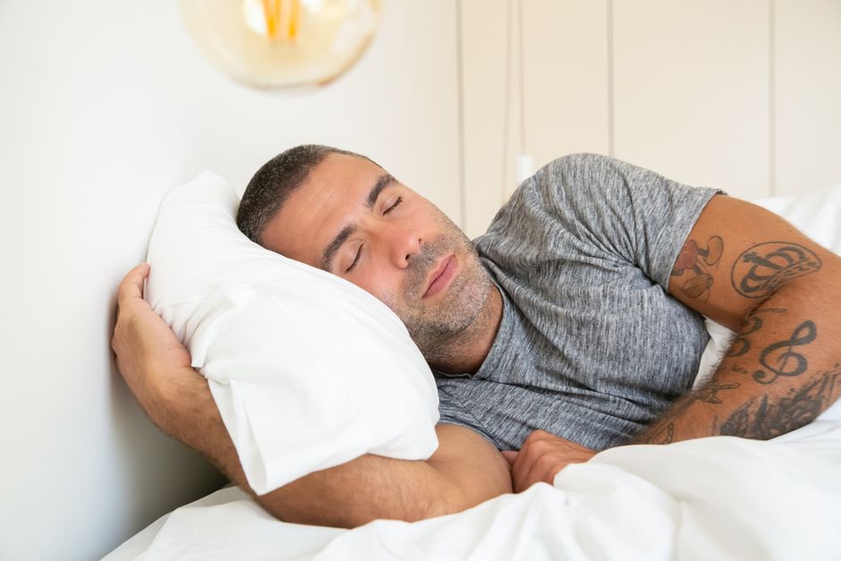 Why Traditional Pillows Fail — What Sleep Science Reveals Man with tattoos resting peacefully in bed, eyes closed, embracing a serene sleep.