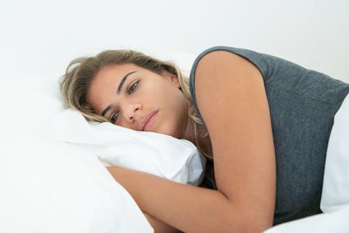 Free Woman in Gray Shirt Lying on the Bed Stock Photo