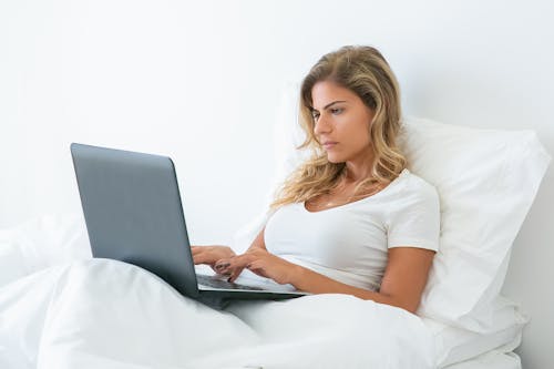 Woman Sitting on Bed While Using Laptop
