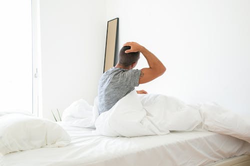 Free Man Sitting on Bed While Stretching His Neck Stock Photo