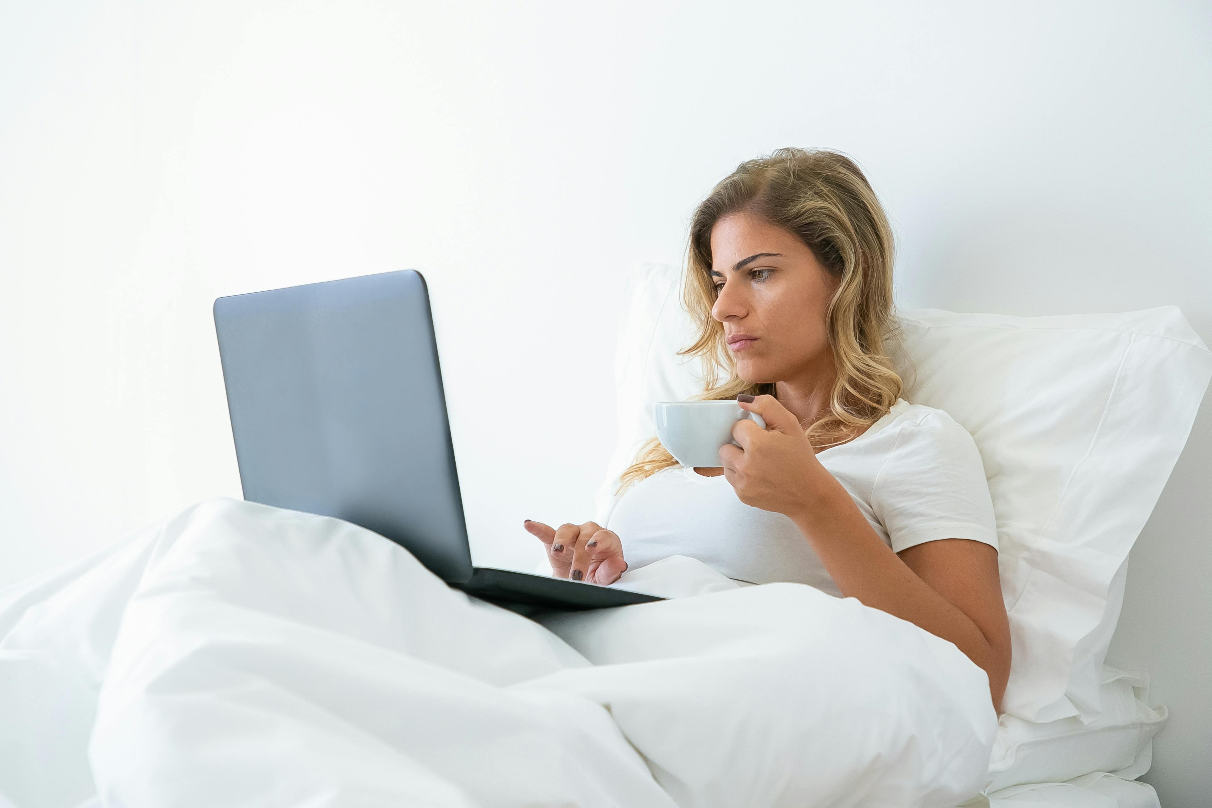 woman in white shirt using laptop while holding a cup