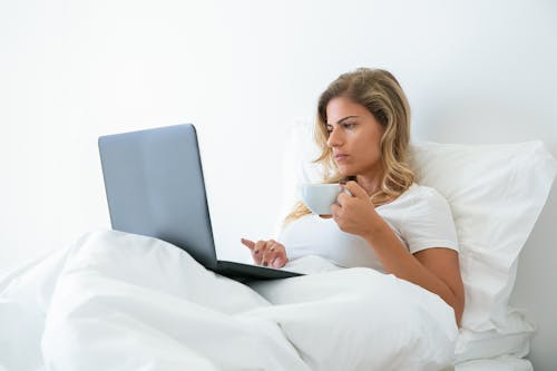 Free Woman in White Shirt Using Laptop While Holding a Cup Stock Photo