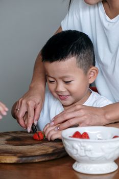 一个年幼的孩子正在成人的指导下学习在木板上切草莓