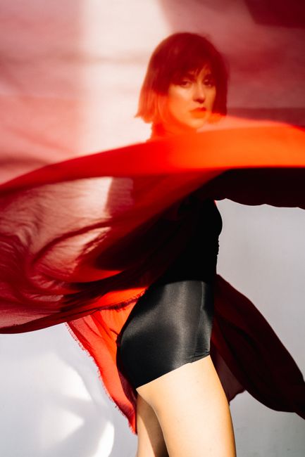 Woman in studio posing with a red scarf and bodysuit captured in motion. Artistic and vivid imagery.