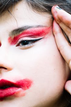 Close-up portrait of a woman with bold red makeup emphasizing eyes and lips, creating a dramatic artistic look.