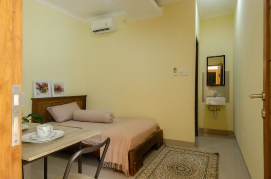A cozy bedroom featuring a wooden bed, air conditioning, and a small dining setup.