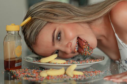 Free A teenage girl playfully interacting with sprinkles and honey on a plate, capturing a whimsical moment. Stock Photo