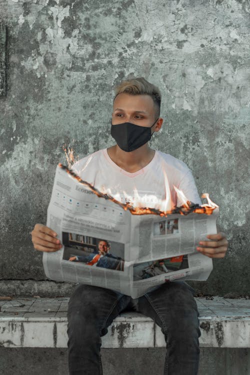 Free Man Wearing Face Mask Holding Newspaper on Fire Stock Photo