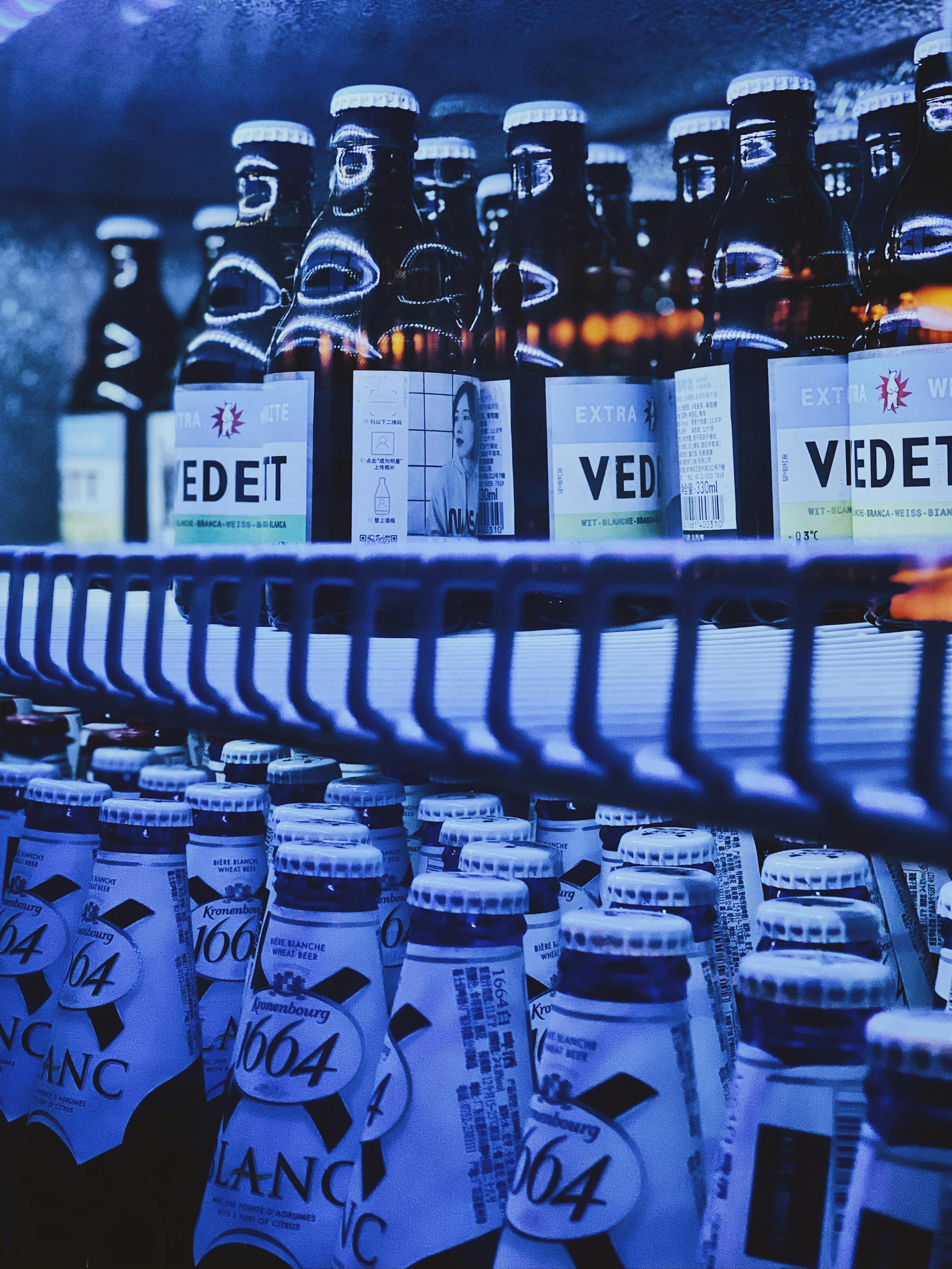 Chilled beer bottles on a refrigerated shelf in a store with a blue ambiance.