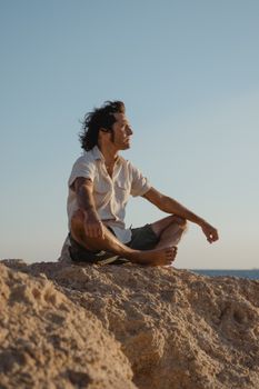 日落时分，一个人以沉思的姿势坐在岩石地形上，享受着宁静的环境