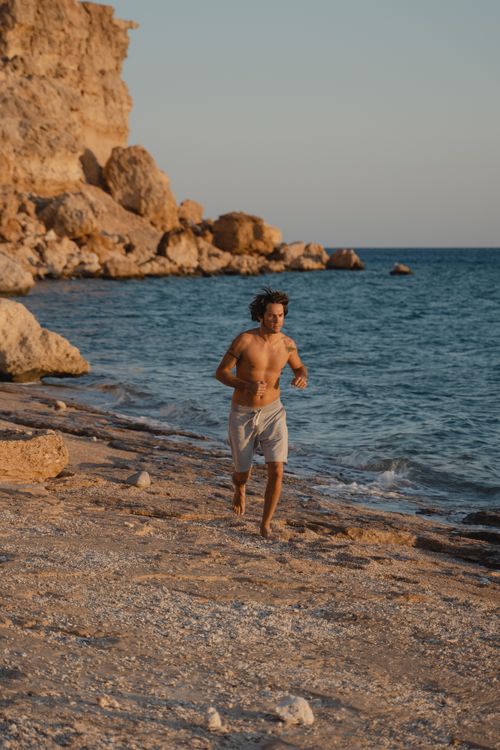 Free A shirtless man runs along a rocky beach during sunset, capturing a sense of freedom and adventure. Stock Photo
