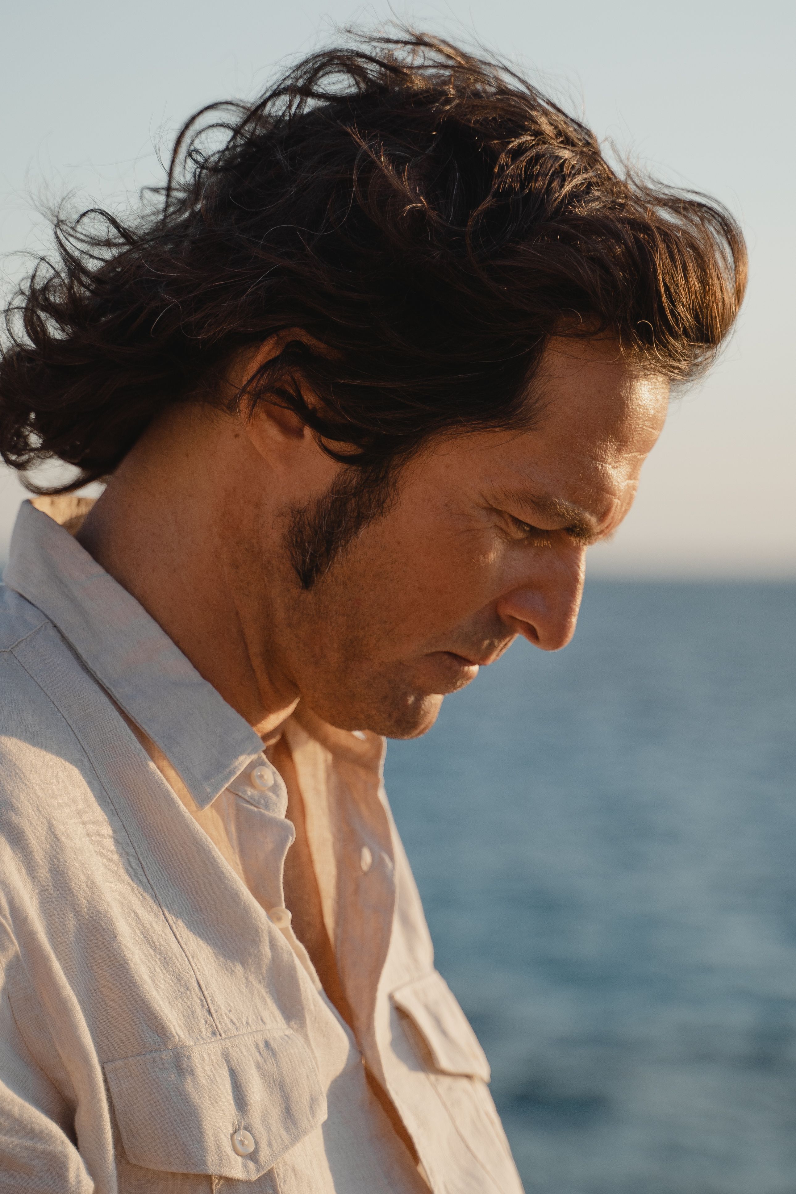 Side view of a man in deep thought outdoors by the sea during sunset.