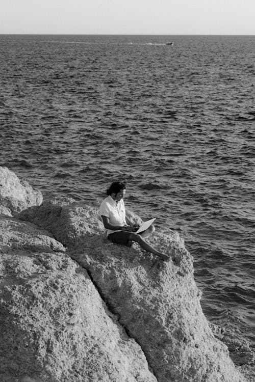 Man Sitting on the Cliff Holding His Laptop