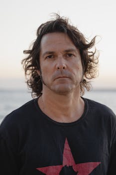 Portrait of a man in a black shirt with star design at the beach during sunset, exuding contemplative mood.