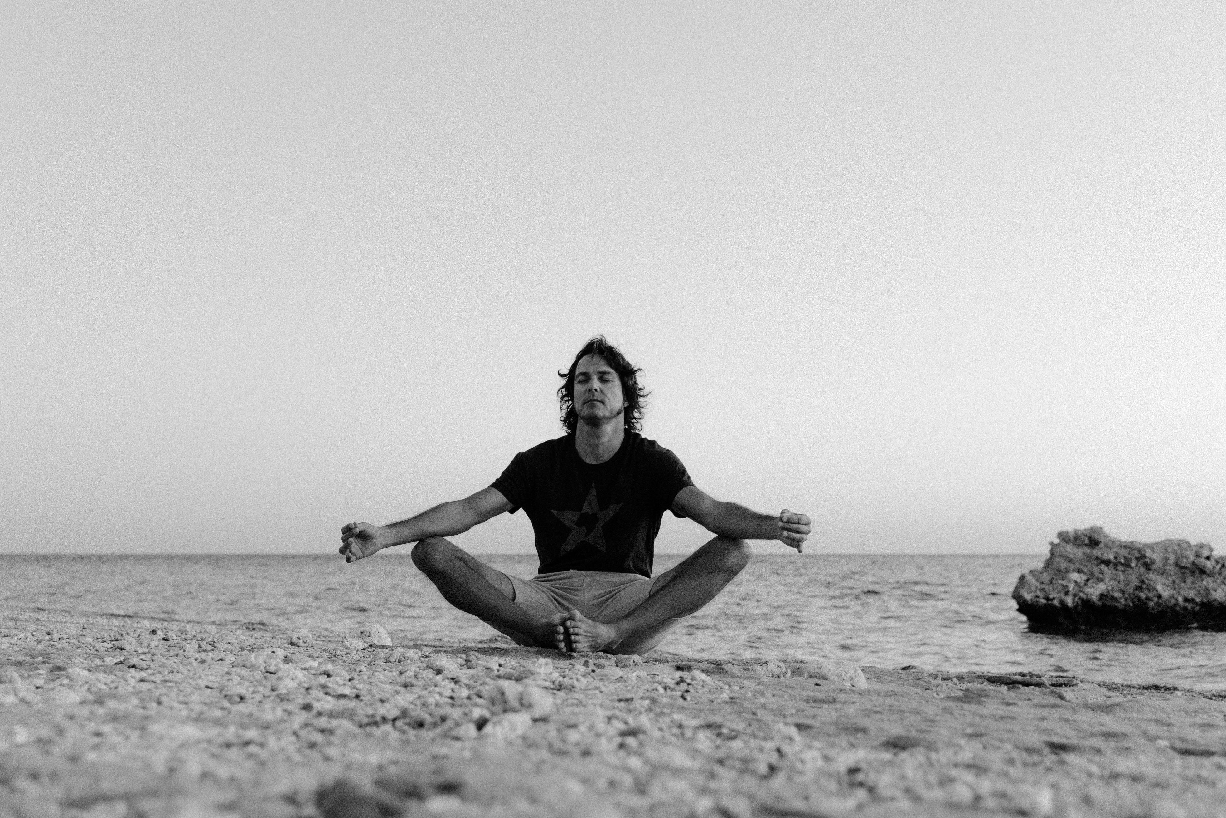 A man meditating on a tranquil beach, captured in black and white, exuding calmness. A man meditating on a tranquil beach, captured in black and white, exuding calmness.