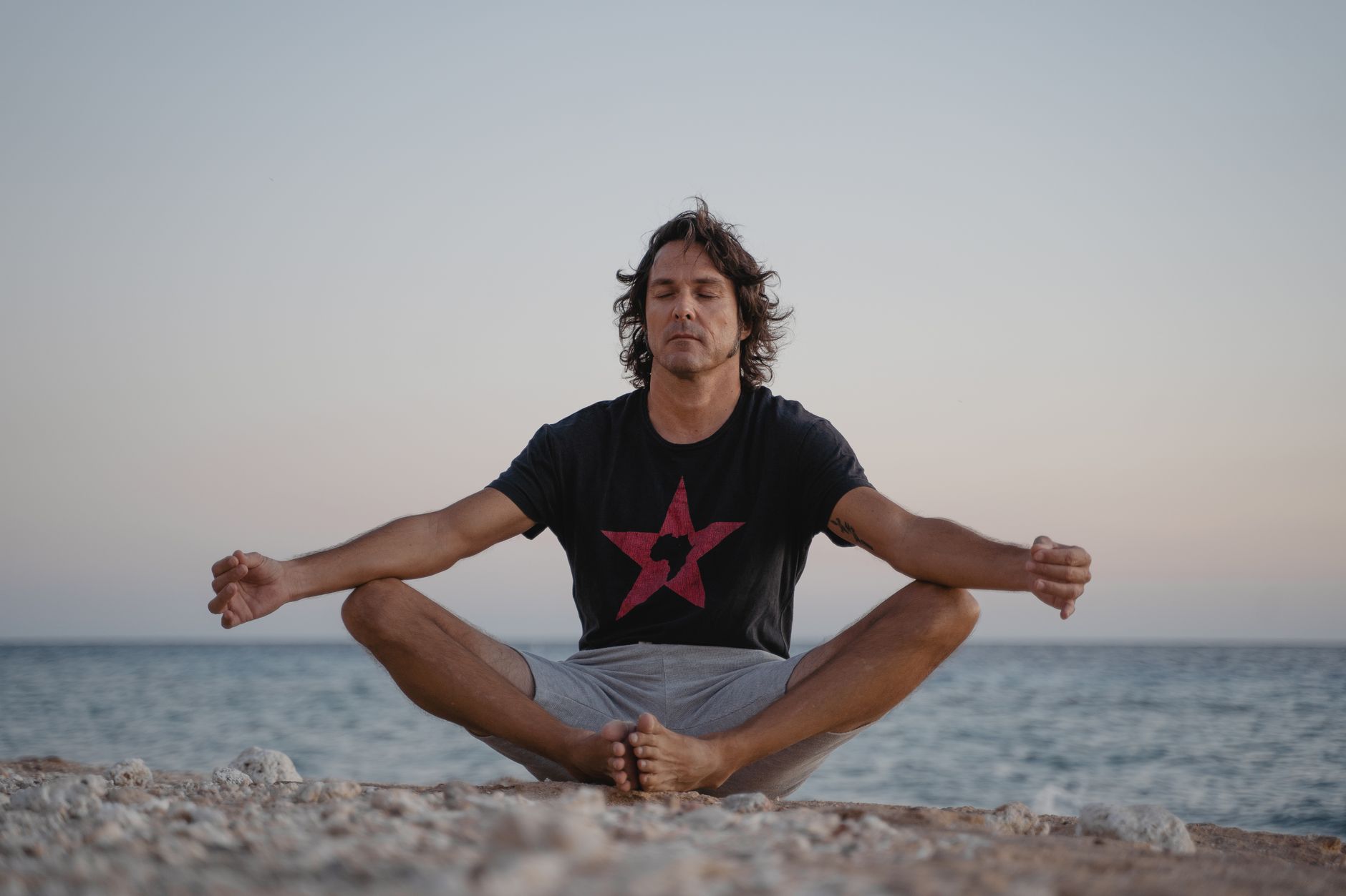 A serene image of a man practicing meditation on a beach, embracing tranquility at the seashore during sunset.