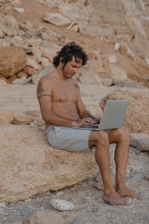 Topless Man Sitting on Rock While Using a Laptop