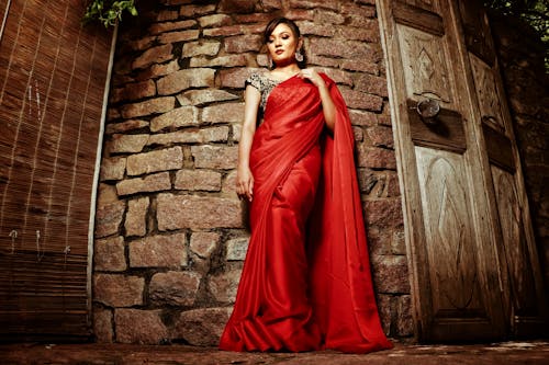 Woman Wearing Red Sari Standing by a Brick Wall