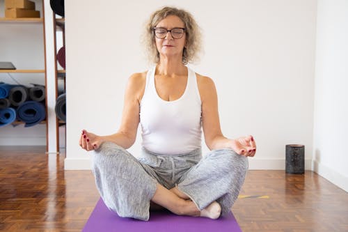 白色背心和灰色的褲子，坐在紫色瑜伽墊上的女人