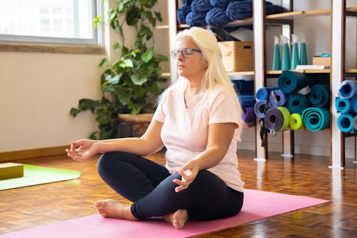 Free Woman in Pink Shirt and Black Leggings Sitting on a Yoga Mat Stock Photo