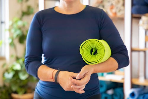 Woman in Blue Long Sleeve Shirt Holding Green Yoga Mat