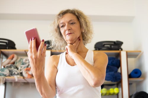 Woman in White Tank Top Holding Pink Smartphone