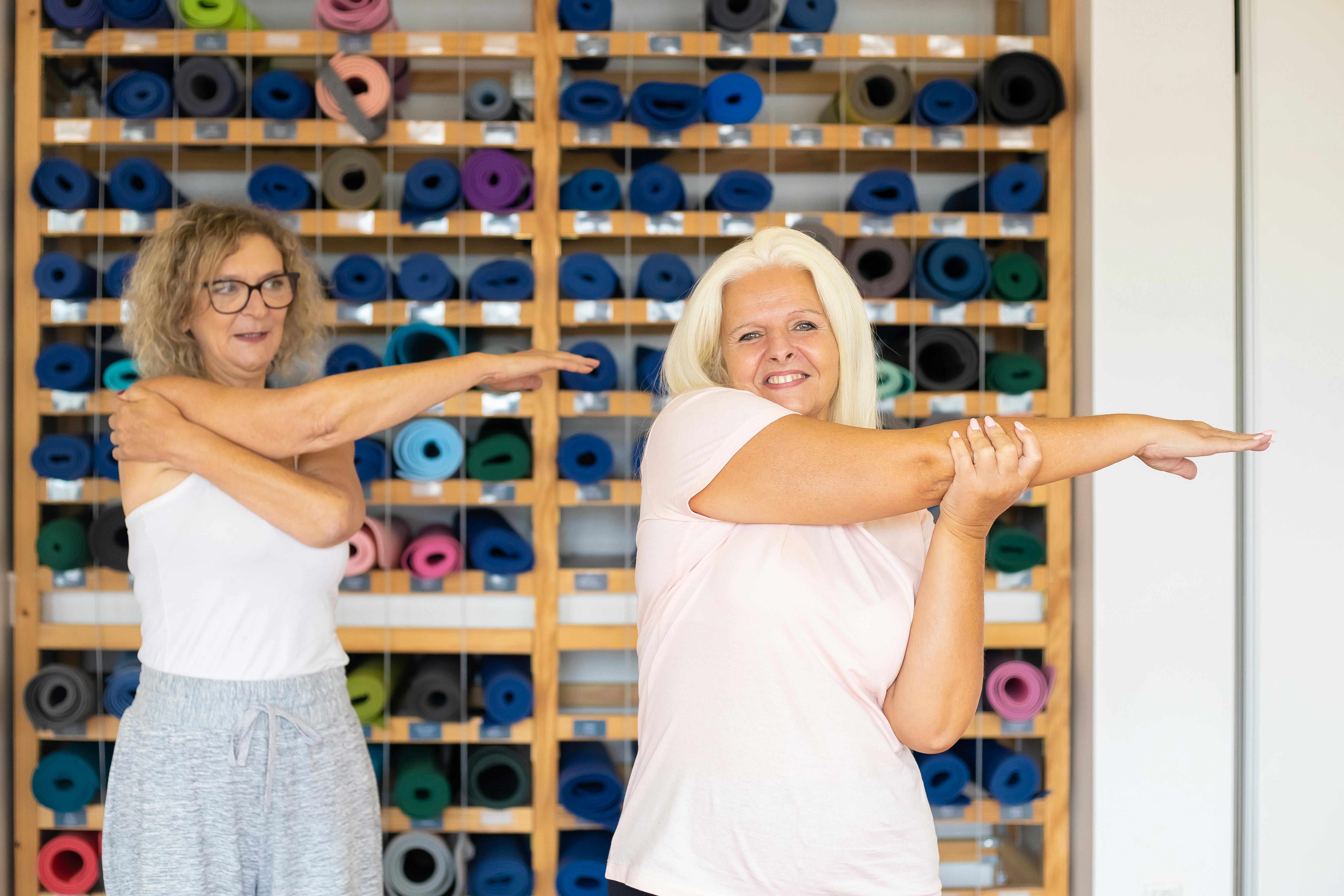 Two women doing arm stretches in a vibrant yoga studio, promoting fitness and wellness.