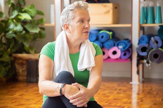Senior woman relaxing after yoga session with yoga mats in the background. Indoor, health-focused setting.
