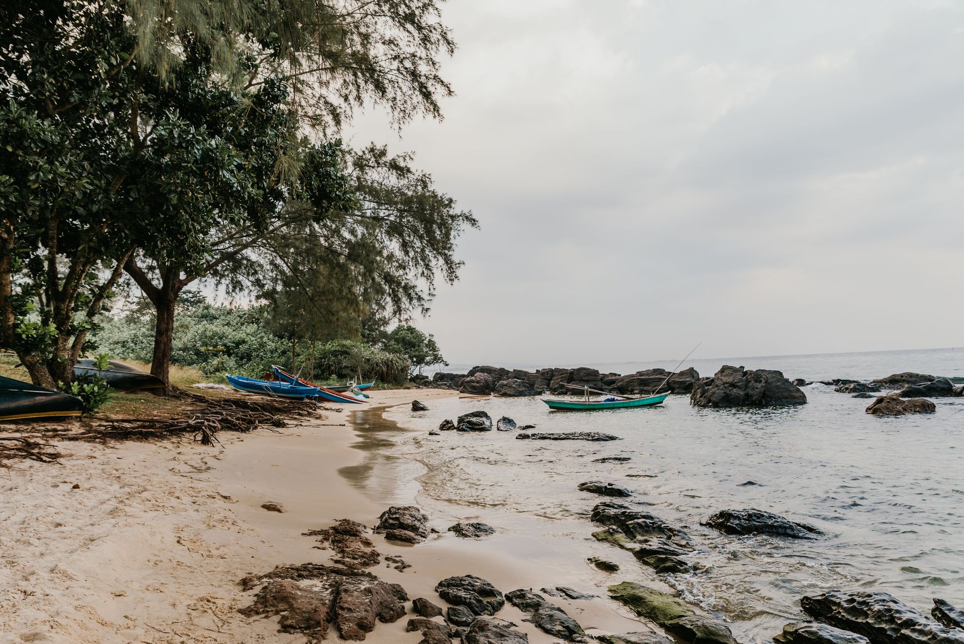 Serene beach scene in Vietnam with fishing boats, rocky shore, and lush trees.