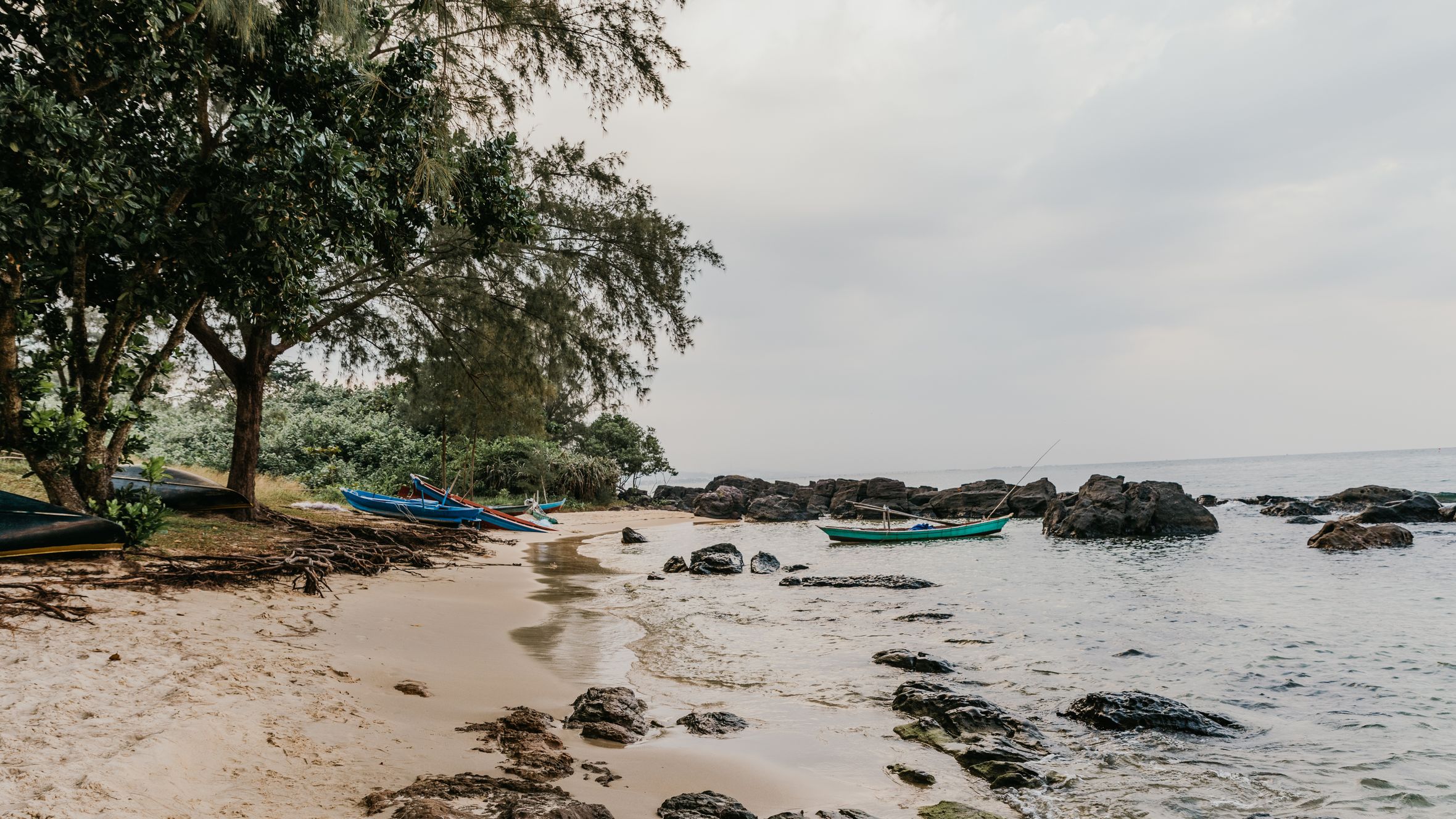 Serene beach scene in Vietnam with fishing boats, rocky shore, and lush trees.