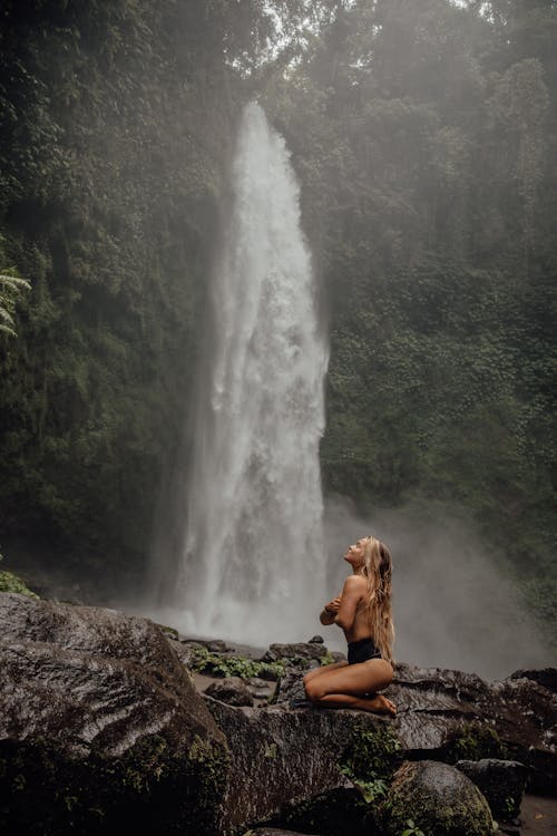 黑色比基尼坐在瀑布附近的岩石上的女人