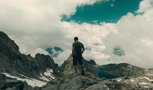 Free A lone hiker stands on a rocky mountain peak in Switzerland, gazing at a tranquil lake below. Stock Photo