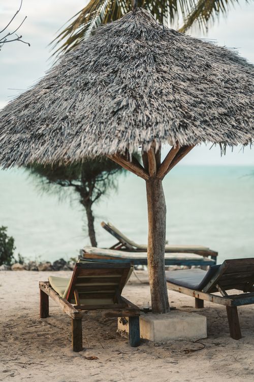 Free Relaxing beach scene with wooden loungers under a thatch sunshade in Zanzibar. Stock Photo