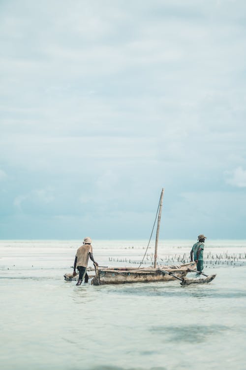 Two Men Dragging Wooden Boat on Sea Shore