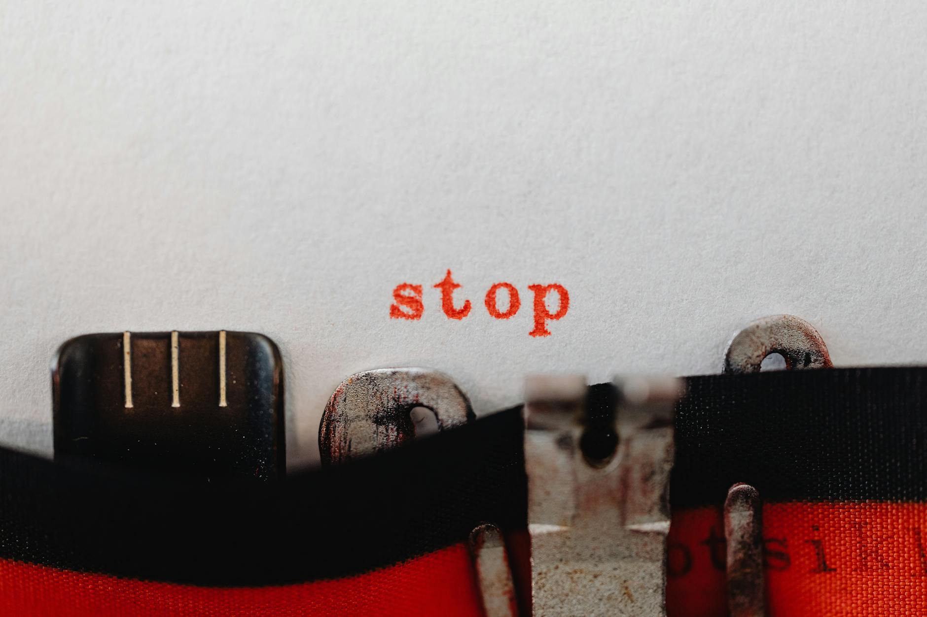 Close-up of a vintage typewriter typing the word 'stop' in red on white paper.
