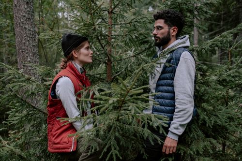 Free Man and woman standing in a forest wearing warm jackets, showcasing outdoor adventure. Stock Photo