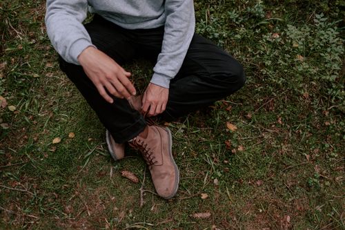 Free Person in casual clothes sitting on grass, wearing brown boots. Stock Photo