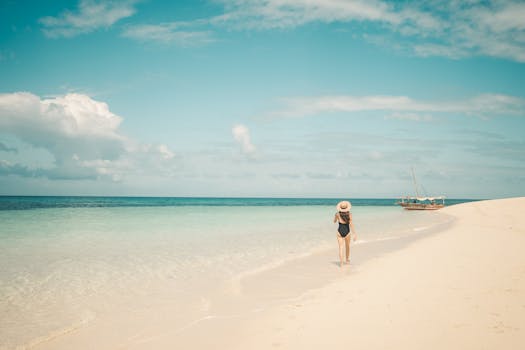 A woman walks along a pristine Zanzibar beach, enjoying a tranquil summer day by the ocean.