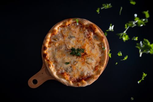 Free Top view of a cheese pizza with herbs on a wooden board against a dark backdrop Stock Photo