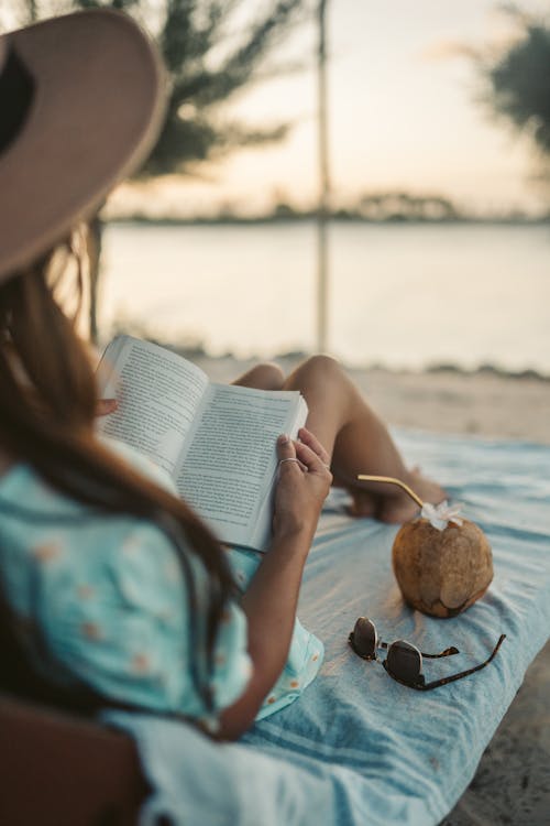 Woman in Blue and White Floral Dress Reading Book on Beach