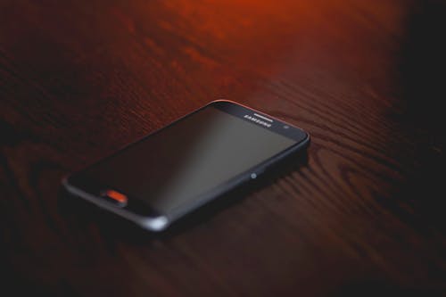 Gratis Smartphone Samsung Hitam Di Permukaan Kayu Coklat Foto Stok