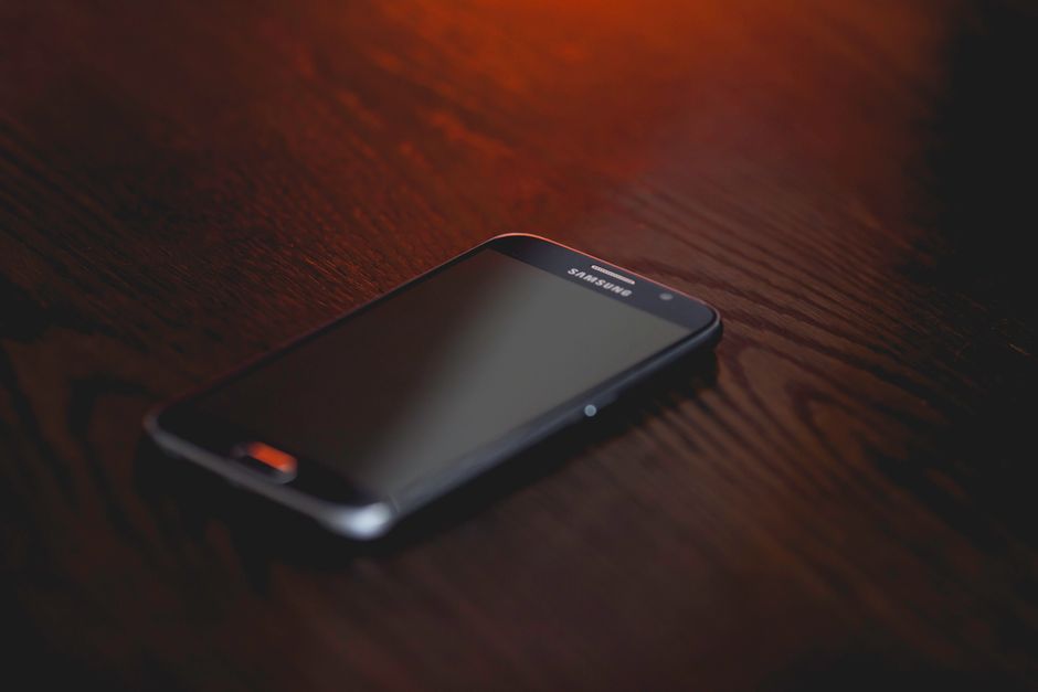 Close-up of a smartphone placed on a dark wooden surface, creating a moody tech ambiance.