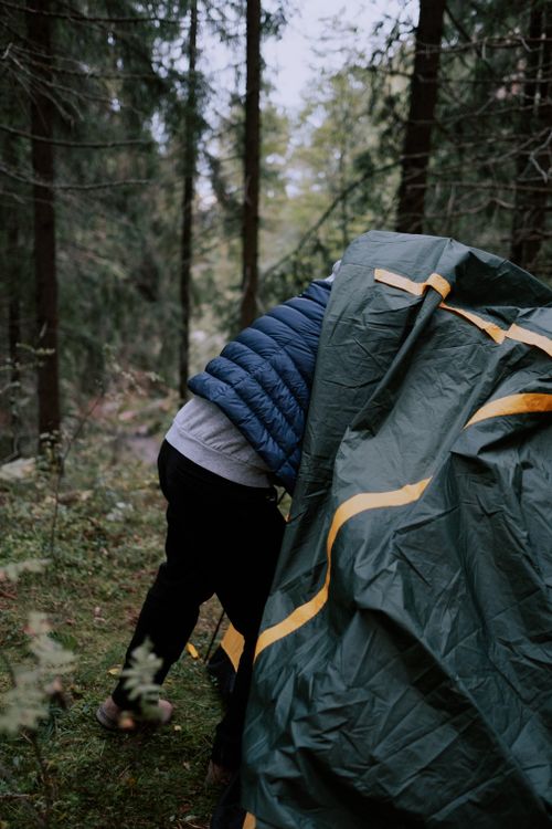 Free A man assembling a tent in a lush green forest, captured during a camping adventure. Stock Photo